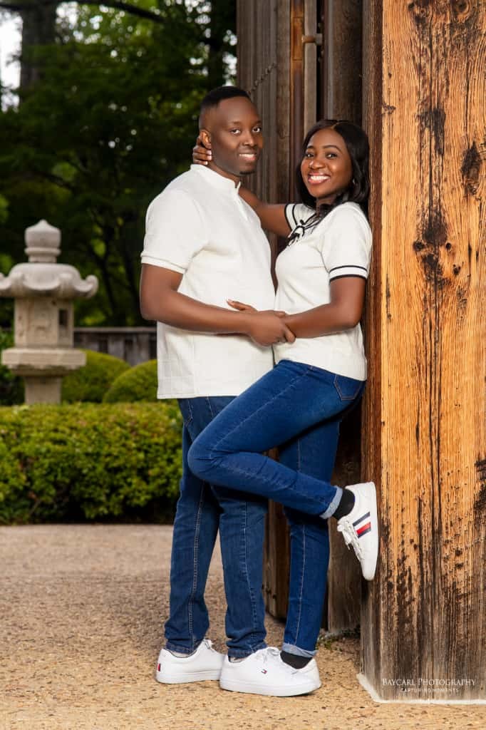 Tolu and Dami in white, smiling beside a wooden gate